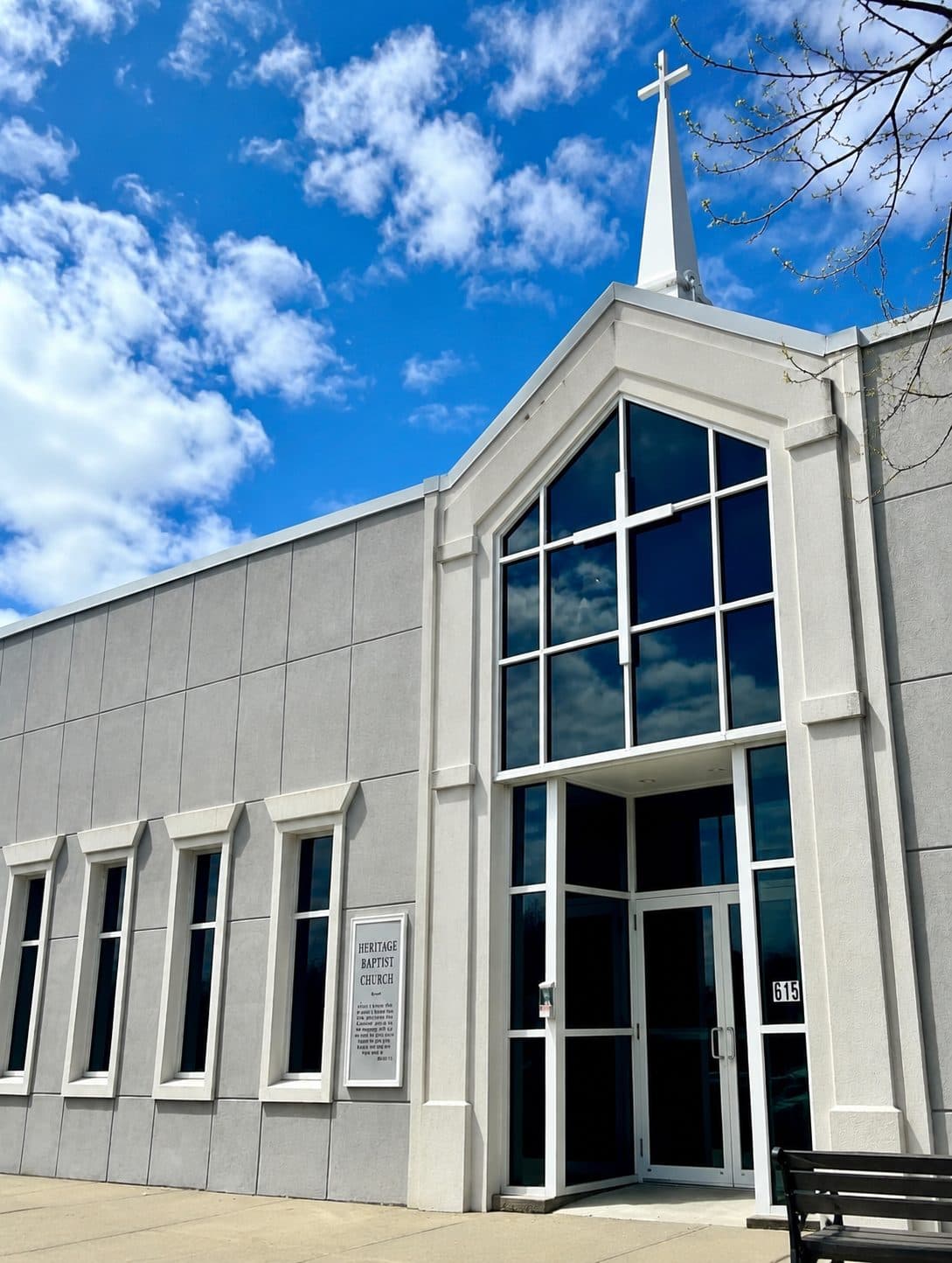 Exterior of Heritage Baptist Church in Norwood, with its white steeple and cross against a blue sky